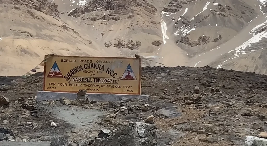 A Border Roads Organisation sign at Shinkula Pass, surrounded by rugged, snow-dusted Himalayan mountains during the Manali to Ladakh road expedition.