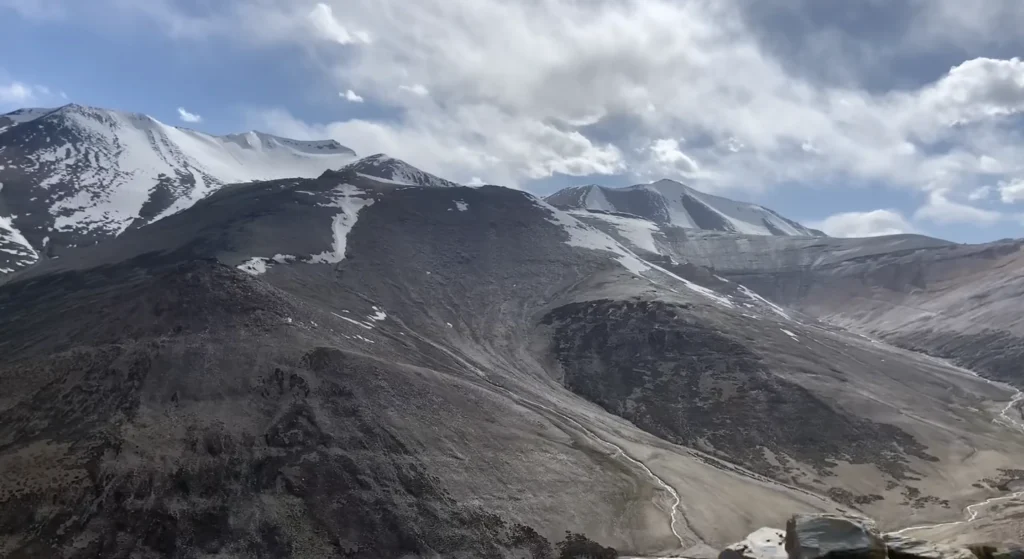 A breathtaking view of rugged, snow-covered Himalayan mountains and a winding high-altitude valley during the Manali to Ladakh road expedition.