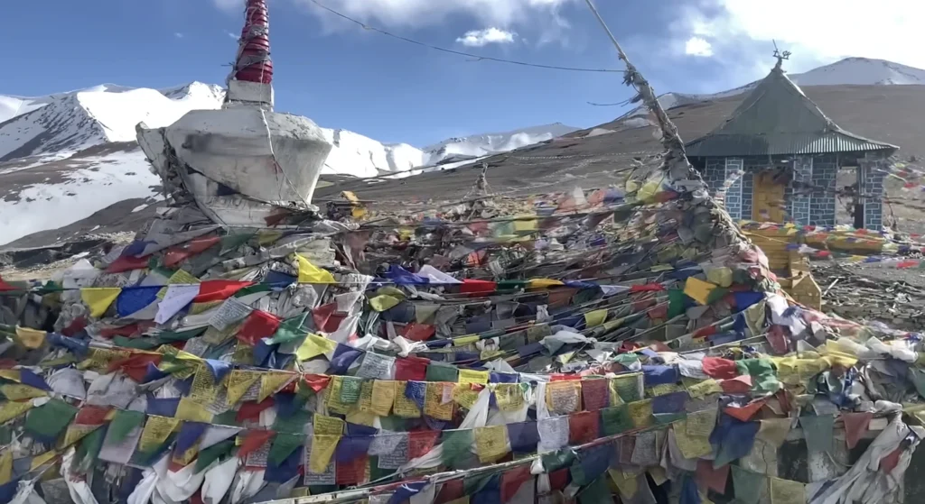 A Buddhist stupa and colorful prayer flags surrounded by snow-covered Himalayan mountains during the Manali to Ladakh road expedition.