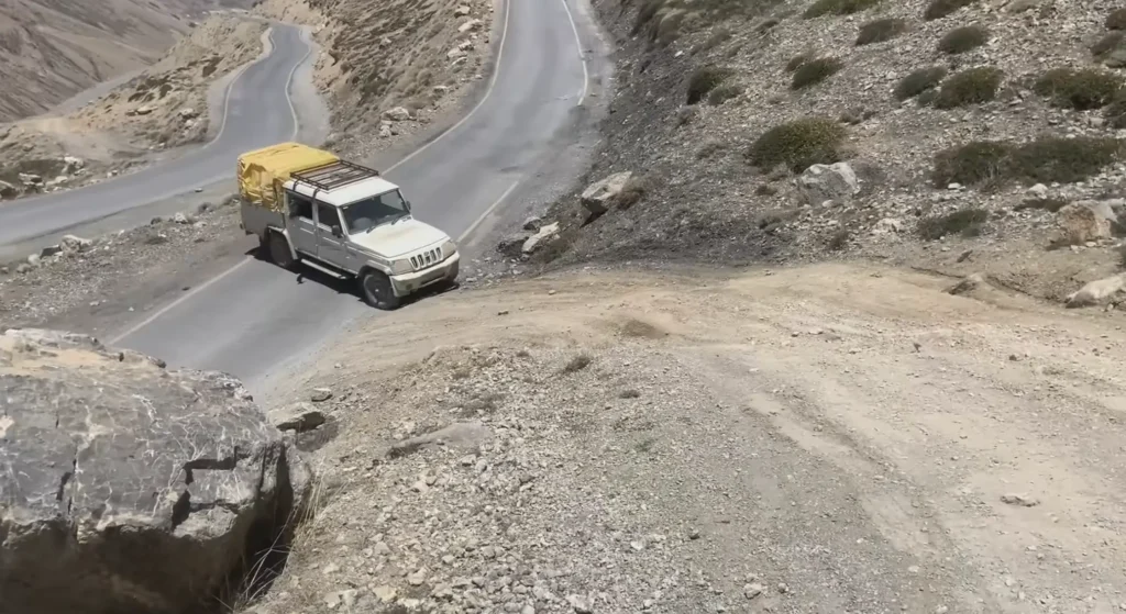 A rugged mountain road with a vehicle navigating a steep winding route through the rocky terrain during the Manali to Ladakh road expedition.