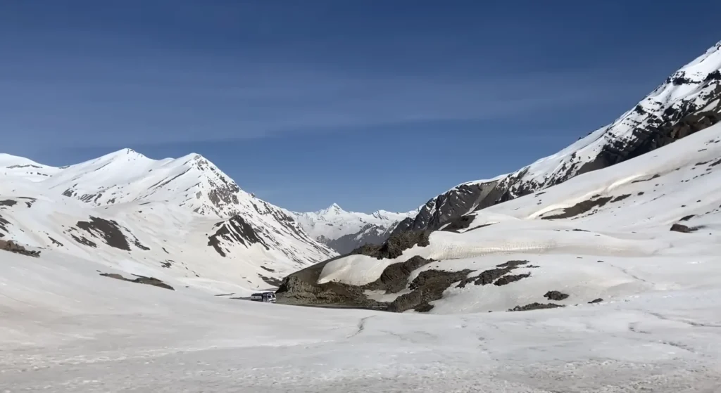 Snow-covered Himalayan mountains and a high-altitude valley along the Manali to Ladakh road expedition under a clear blue sky.