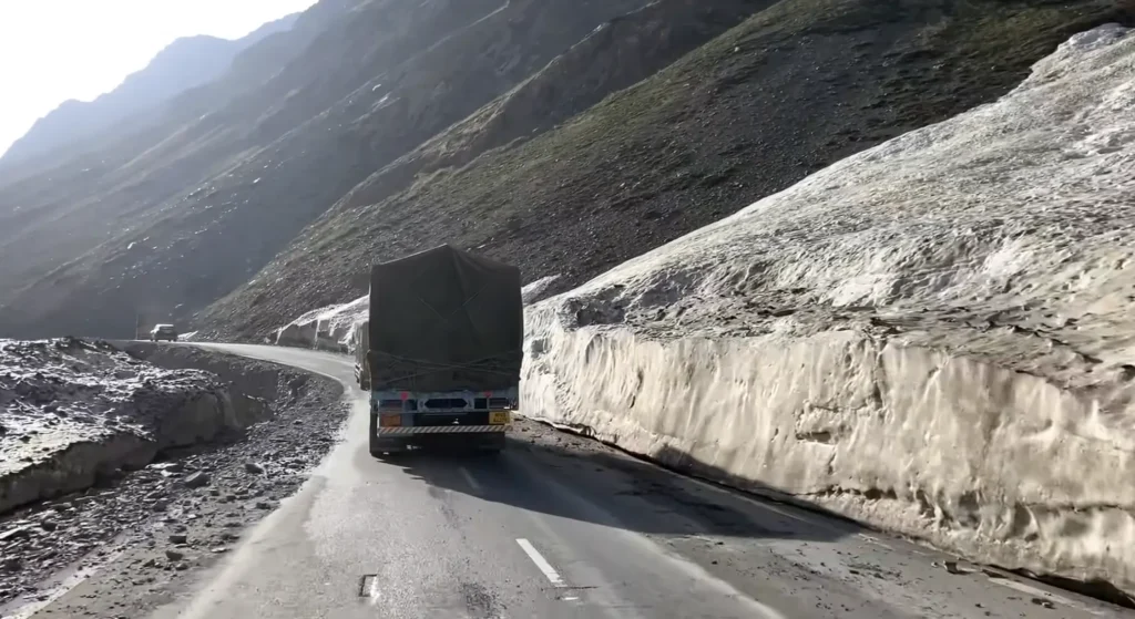 A truck navigates a narrow mountain road surrounded by snow-covered slopes during a Manali to Ladakh road expedition.